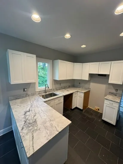 Completed custom kitchen cabinet installation with white cabinetry and stone wall.